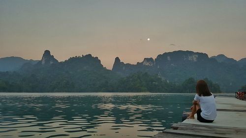 Man on lake against sky during sunset