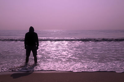 Rear view of man on beach against sky during sunset