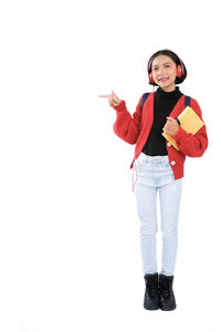 Portrait of smiling girl pointing while holding book against white background