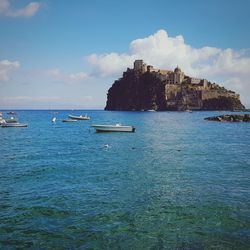 Sailboats in sea against sky with historic building on background 