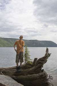 Full length of teenage boy standing on driftwood against lake at wells gray provincial park