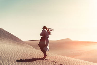 Full length of woman standing on sand at beach against clear sky