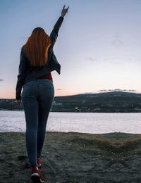 Rear view of woman standing at beach against sky