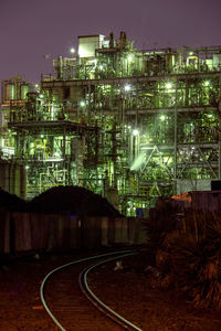 Illuminated railroad tracks by buildings against sky at night