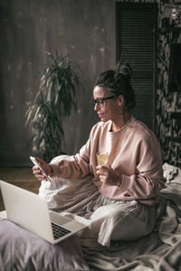 Young woman using mobile phone while sitting on bed