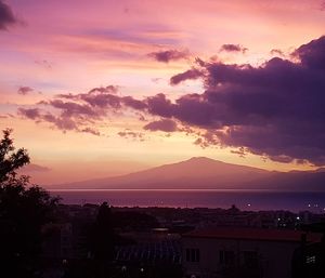 Silhouette of city against cloudy sky during sunset