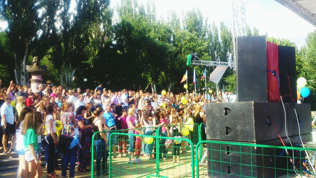 tree, men, person, lifestyles, leisure activity, large group of people, green color, day, sunlight, outdoors, chair, built structure, childhood, grass, incidental people, fence, park - man made space, casual clothing, playground