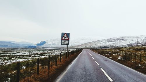 Road sign on landscape against sky