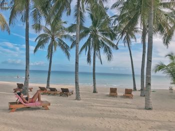 Lounge chairs and palm trees on beach against sky