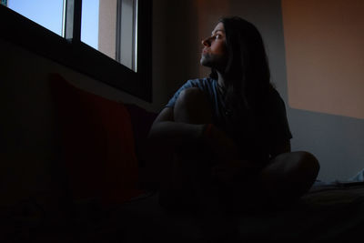 Woman sitting while looking through window at home