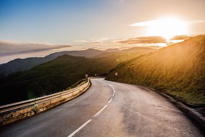 Diminishing perspective of empty road amidst mountains against sky during sunset