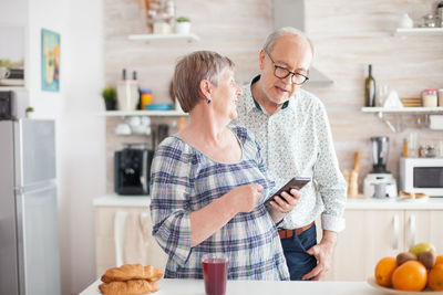 Woman using phone by man while standing in kitchen at home