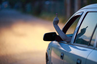 Cropped hand showing obscene gesture from car on road