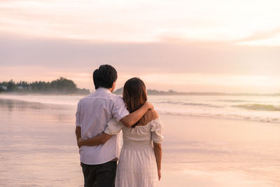 Couple standing on shore against sky during sunset