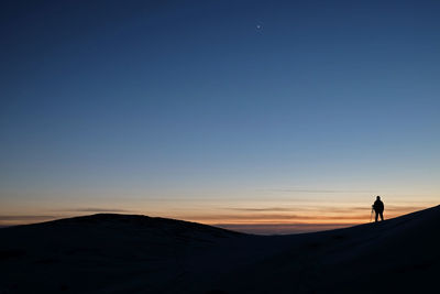 Silhouette man walking on desert against clear sky during sunset