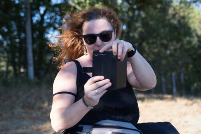 Woman wearing sunglasses using smart phone while sitting outdoors