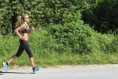 Full length of woman running on road by trees