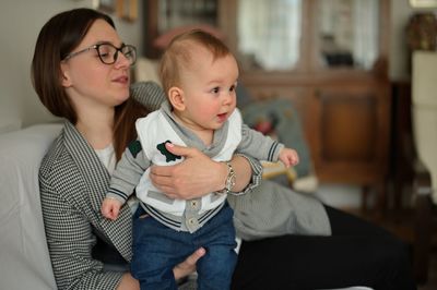 Cute little baby holding by his mother relaxing on a sofa