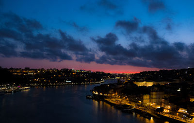 Illuminated buildings by river against sky at night