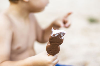 Midsection of shirtless boy holding ice cream at beach