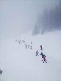 People skiing on snow covered field during foggy weather