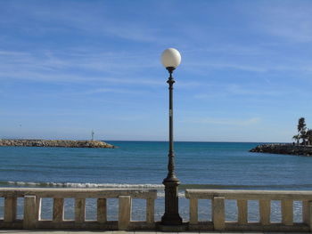 Street light by sea against blue sky