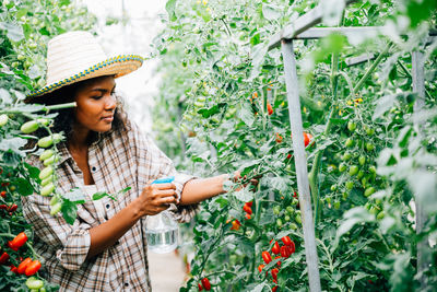 Young woman using mobile phone while standing against plants