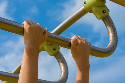 Low angle view of hand holding metal against sky