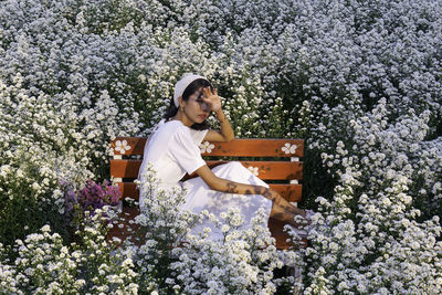 Portrait of young woman sitting on bench sitting amidst plants