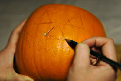 Cropped hands marking on pumpkin during halloween