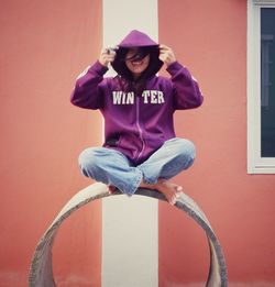 Rear view of young woman with arms raised standing against wall