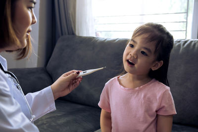 Doctor examining girl temperature at home