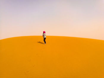 Woman standing on sand dune against sky at desert