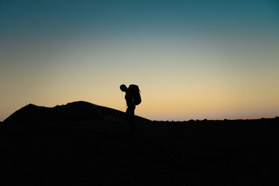 Silhouette man walking on mountain against clear sky during sunset