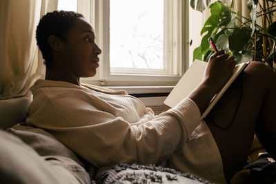 Woman writing in book while reclining on bed at home