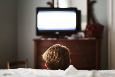 Rear view of boy looking through camera at home