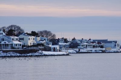 Houses by sea against sky during sunset