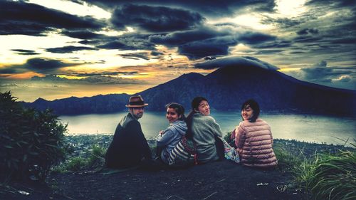 People sitting on mountain against sky during sunset