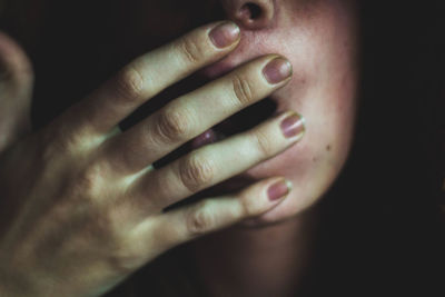 Cropped image of young woman covering face against black background