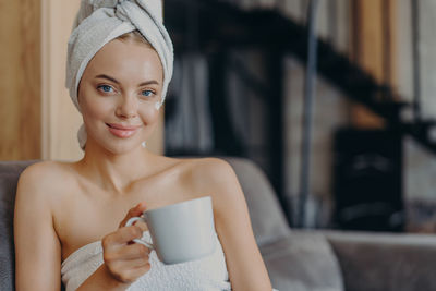 Portrait of smiling young woman holding coffee cup sitting at home