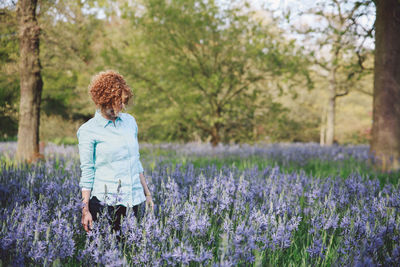 Woman standing amidst purple flowering plants at forest