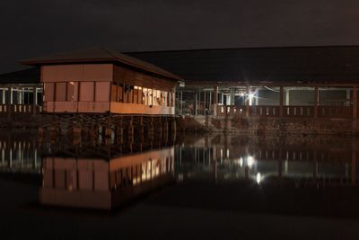 Illuminated building by lake against sky at night