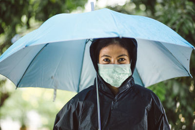 Portrait of woman wearing mask and raincoat holding umbrella whole standing outdoors