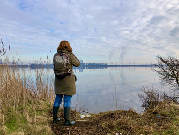 Rear view of man photographing lake against sky