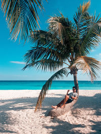 Woman sitting on palm tree at beach against sky