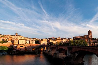 Bridge over river by buildings in city against sky