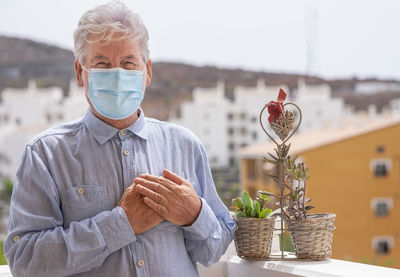 Portrait of senior man wearing mask standing against buildings