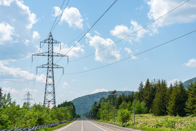Electricity pylon by road against sky