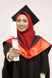 Young woman in graduation gown standing against white background