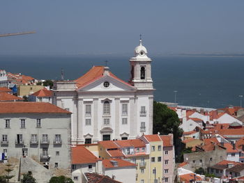 Buildings in town by sea against sky